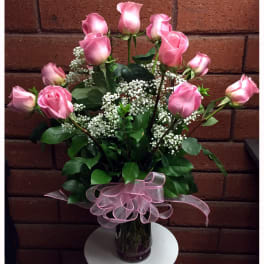 Pink roses arranged in a glass vase with baby's breath and a pink ribbon