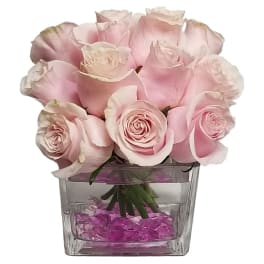 Pink roses arranged in a clear square vase with purple stones