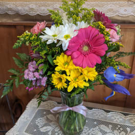 Mixed bouquet in a glass vase with pink, yellow, white, and blue flowers