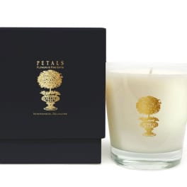 White candle in a glass tumbler beside a black gift box