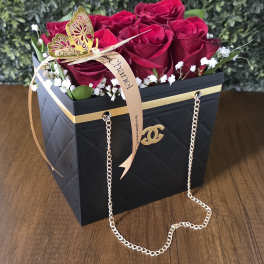 Red roses in a black gift box with a gold ribbon and chain handle