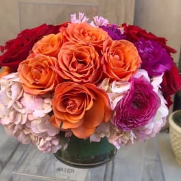 Round bouquet of orange, red, pink, and purple flowers in a glass vase
