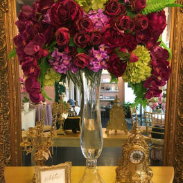 Large floral arrangement in a clear glass vase with burgundy, purple, and lime blooms