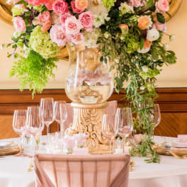 Large pink and white floral centerpiece in a clear vase on a decorated table