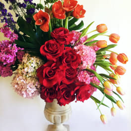 Mixed bouquet of red roses, orange tulips, and pink hydrangeas in a stone vase