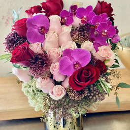 Bouquet of red and pink roses with purple orchids in a gold vase
