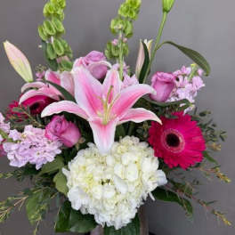 Pink lilies and mixed blooms arranged in a silver vase