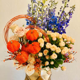 Bouquet of cream roses and blue delphinium with orange pumpkin accents in a gold vase
