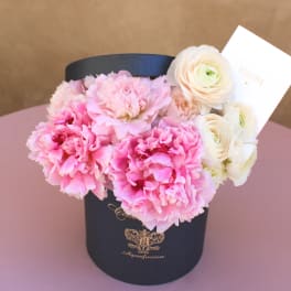 Pink carnations and white ranunculus in a black hat box