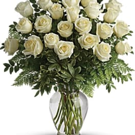 White roses arranged in a clear glass vase with greenery
