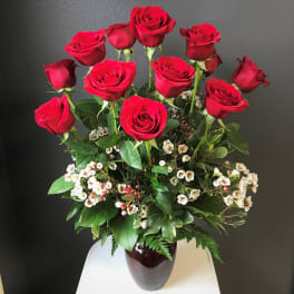 Red roses arranged in a dark vase with white filler flowers