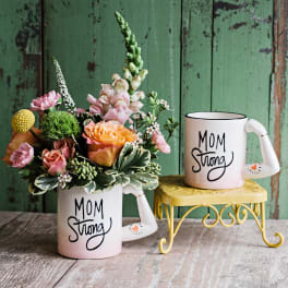 Floral arrangement in a mug with a matching "Mom Strong" mug beside it