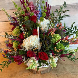 Large mixed flower arrangement with red roses, white hydrangea, and purple accents in a white basket
