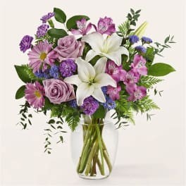 Lavender and white bouquet with lilies, roses, daisies, and alstroemeria in a clear glass vase.
