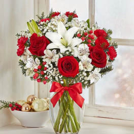 Red roses and white lilies in a clear glass vase with a red ribbon