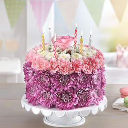Pink floral cake with striped birthday candles on a white stand