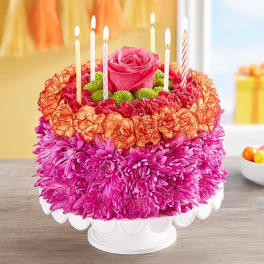 Round floral cake with candles and a pink rose topper