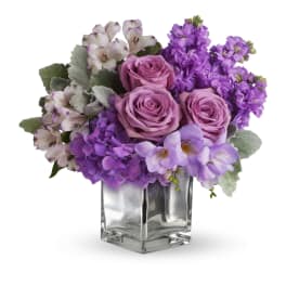 Purple roses and lavender flowers arranged in a clear glass vase