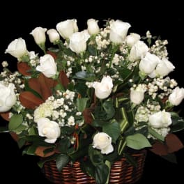 Basket arrangement of white roses and white berries in a brown basket against a black background