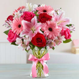 Bouquet of pink and red flowers in a glass vase with a pink ribbon