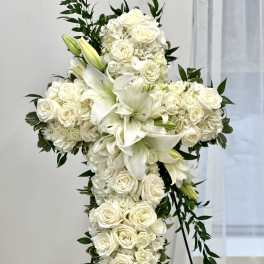 White floral cross on a stand with lilies and roses