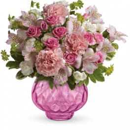 Pink carnations, spray roses, and white alstroemeria in a round pink glass vase