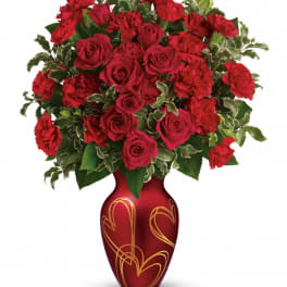 Arrangement of red roses and carnations in a red vase with gold heart designs
