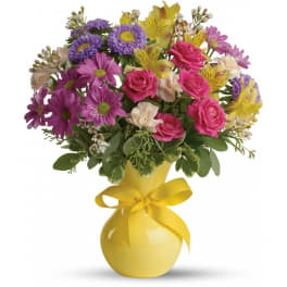 Bright mixed bouquet of pink roses, purple daisies and yellow blooms in a yellow vase with ribbon