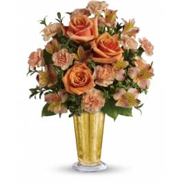 Arrangement of orange roses and peach carnations with alstroemeria in a tall gold glass vase.