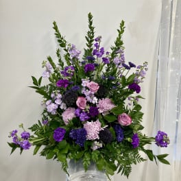 Tall purple and pink floral arrangement in a white pedestal vase
