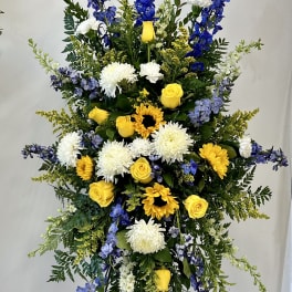 Tall standing floral spray with yellow roses, white mums, and blue delphinium