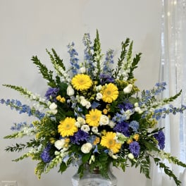 Large floral arrangement with yellow daisies, white roses, and blue-purple flowers in a vase
