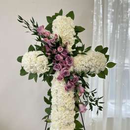 White floral cross with pink roses and greenery on a stand