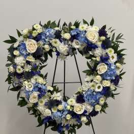 Heart-shaped floral wreath with blue, white, and cream flowers on a stand