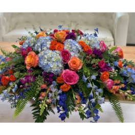 Large colorful floral centerpiece with roses and blue hydrangeas on a table