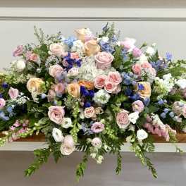 Large pastel floral casket spray with roses and blue blooms