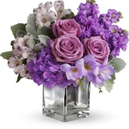 Lavender roses and purple flowers arranged in a clear square vase