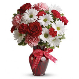 Red and pink flowers arranged in a red vase with a polka-dot ribbon