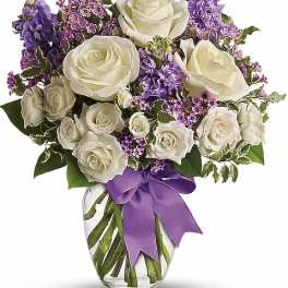 Clear vase of white roses and purple flowers tied with a purple ribbon bow