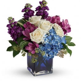 Bouquet of white roses, blue hydrangeas, and purple flowers in a blue glass vase