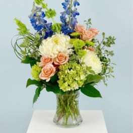 Mixed bouquet in a clear glass vase with blue, peach, and white blooms