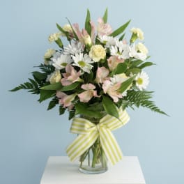 Bouquet of white daisies and pink alstroemeria in a glass vase with a striped ribbon