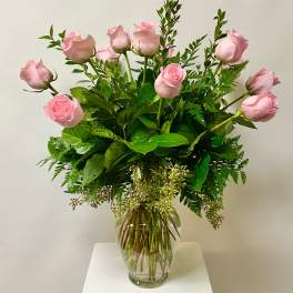 Pink roses arranged in a clear glass vase with lush greenery.