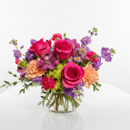Mixed bouquet of pink and purple flowers in a round glass vase