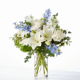 White lilies and roses with blue flowers in a clear glass vase