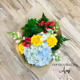 Wrapped bouquet with yellow roses, blue hydrangeas, white blooms, and red berries