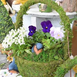 Moss-covered basket with purple and white pansies and small bird figurines