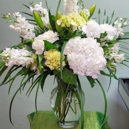 White floral arrangement in a clear glass vase with long green leaves