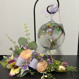 Pastel floral arrangement with roses and purple accents beside a hanging glass ornament
