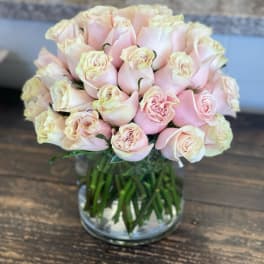 Compact arrangement of pale pink roses clustered in a clear glass cylinder vase
